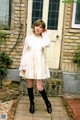 A woman in a white dress and black boots standing in front of a door.