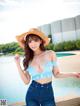 A woman in a blue top and a straw hat posing by a pool.