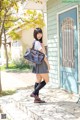 A woman in a school uniform is standing outside of a house.