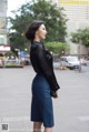 A woman in a black shirt and blue skirt is standing on the street.